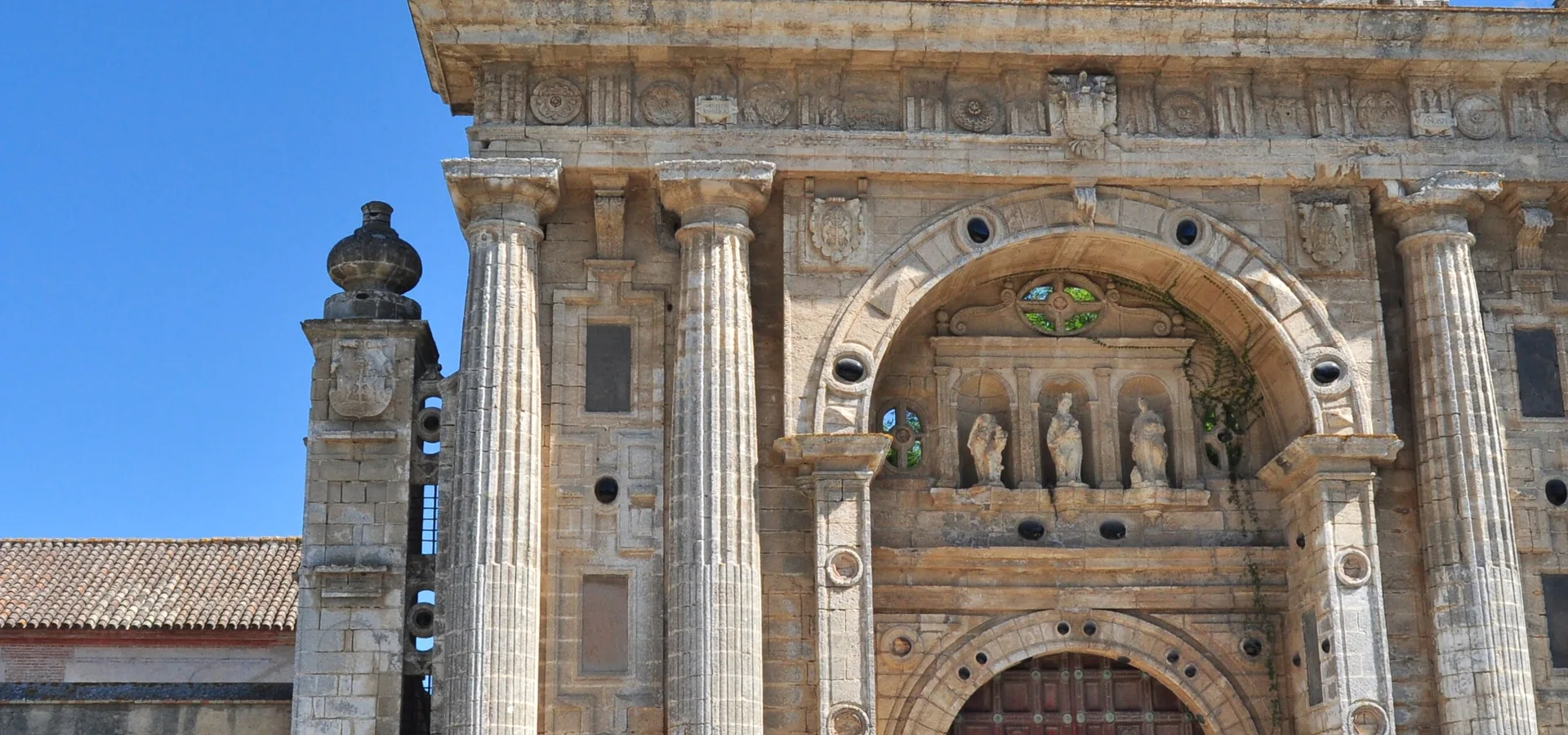 The Renaissance gateway of the Charterhouse of Jerez, with its columns and carved pediment, in a sunlit courtyard; a general photograph of the monastery beside the stud farm